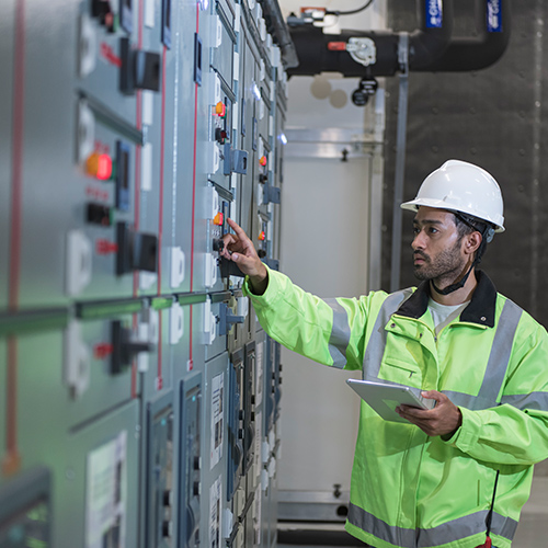 man with clipboard in yellow jacket inspecting commercial electrical panel 