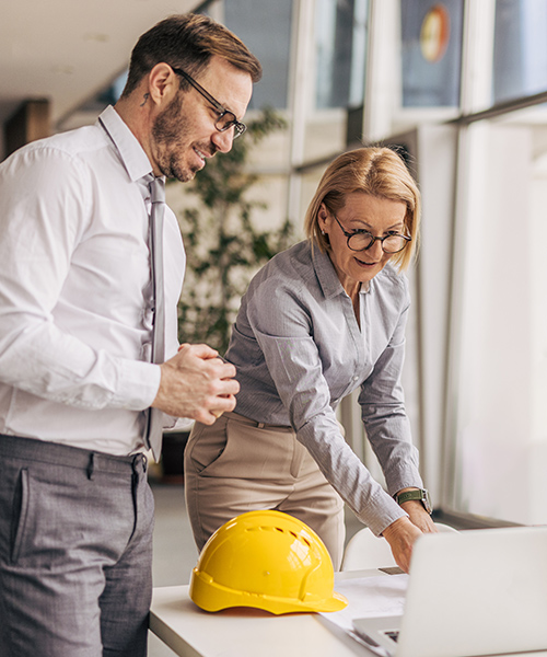 two people looking at plans and a laptop on a desk