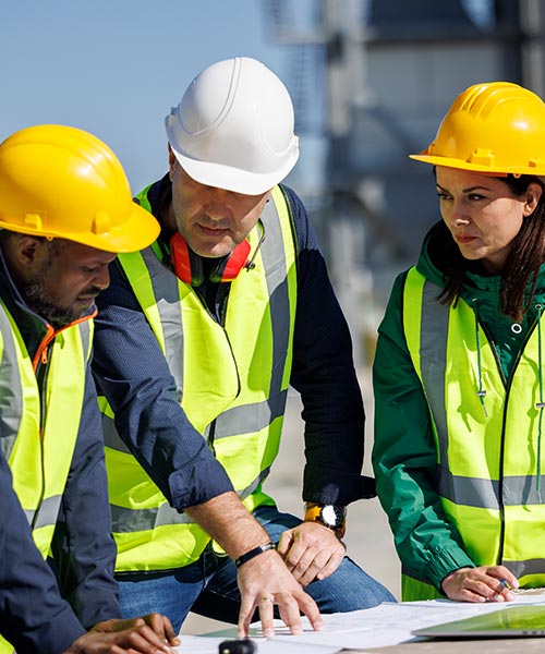 three people on a construction site wearing hard hats looking over plans