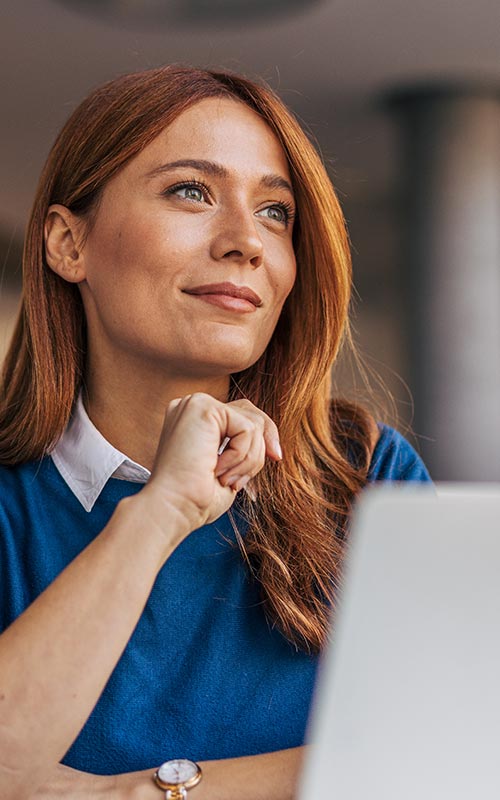 woman sitting at desk with laptop thoughfully staring into the distance