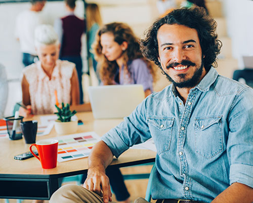 man sitting comfortably at a desk with colleagues around smiling